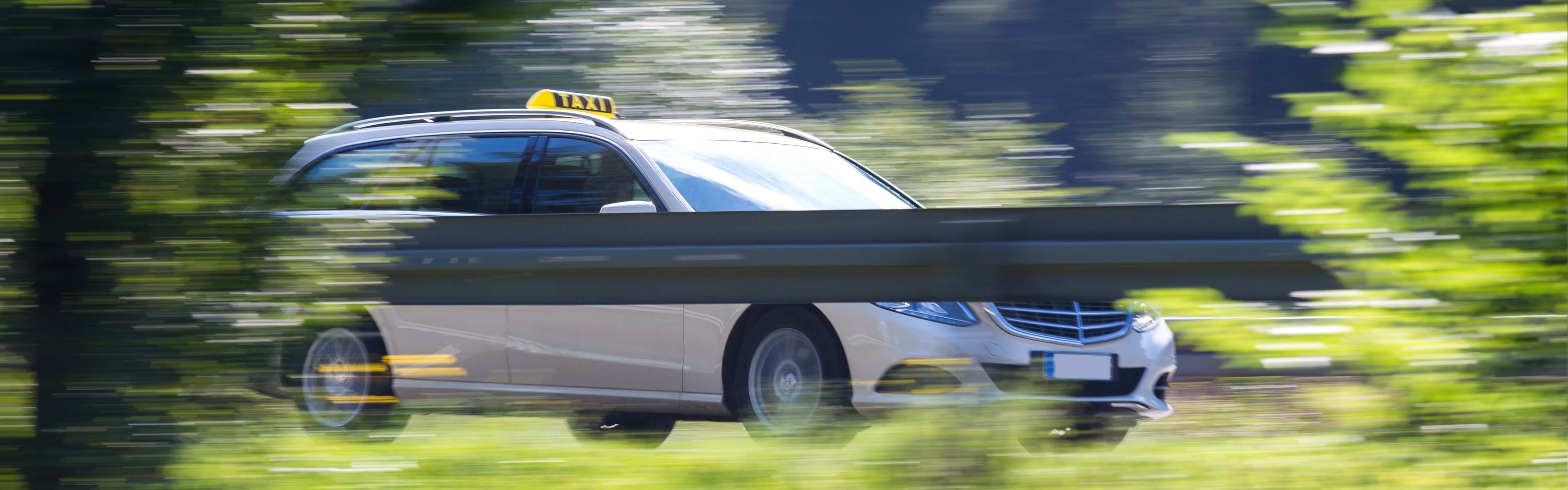 Taxi fährt auf einer Straße, verschwommene Pflanzen im Vordergrund