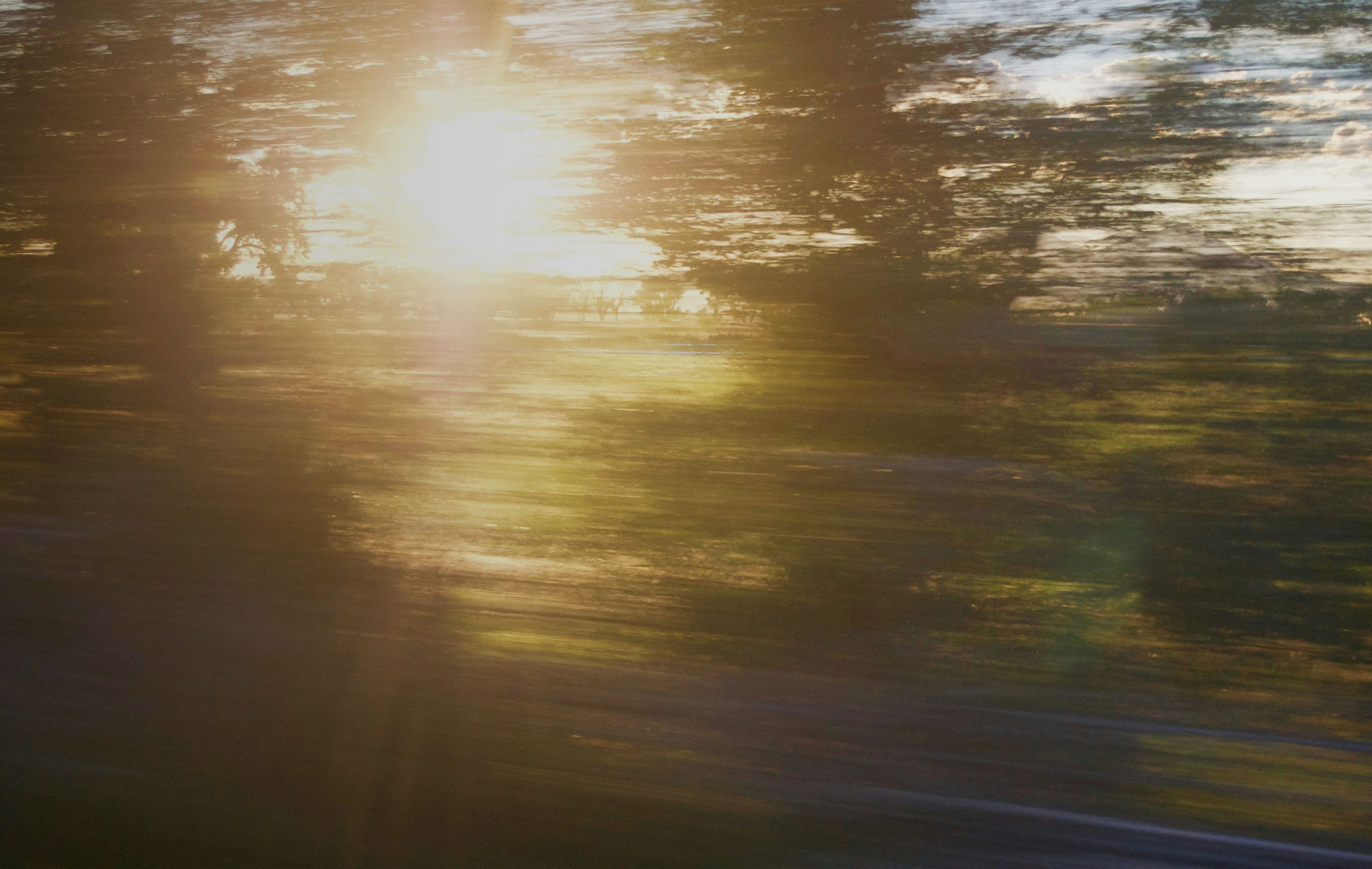 Sonnenuntergang durch verschwommene Landschaft, fotografiert aus einem fahrenden Fahrzeug