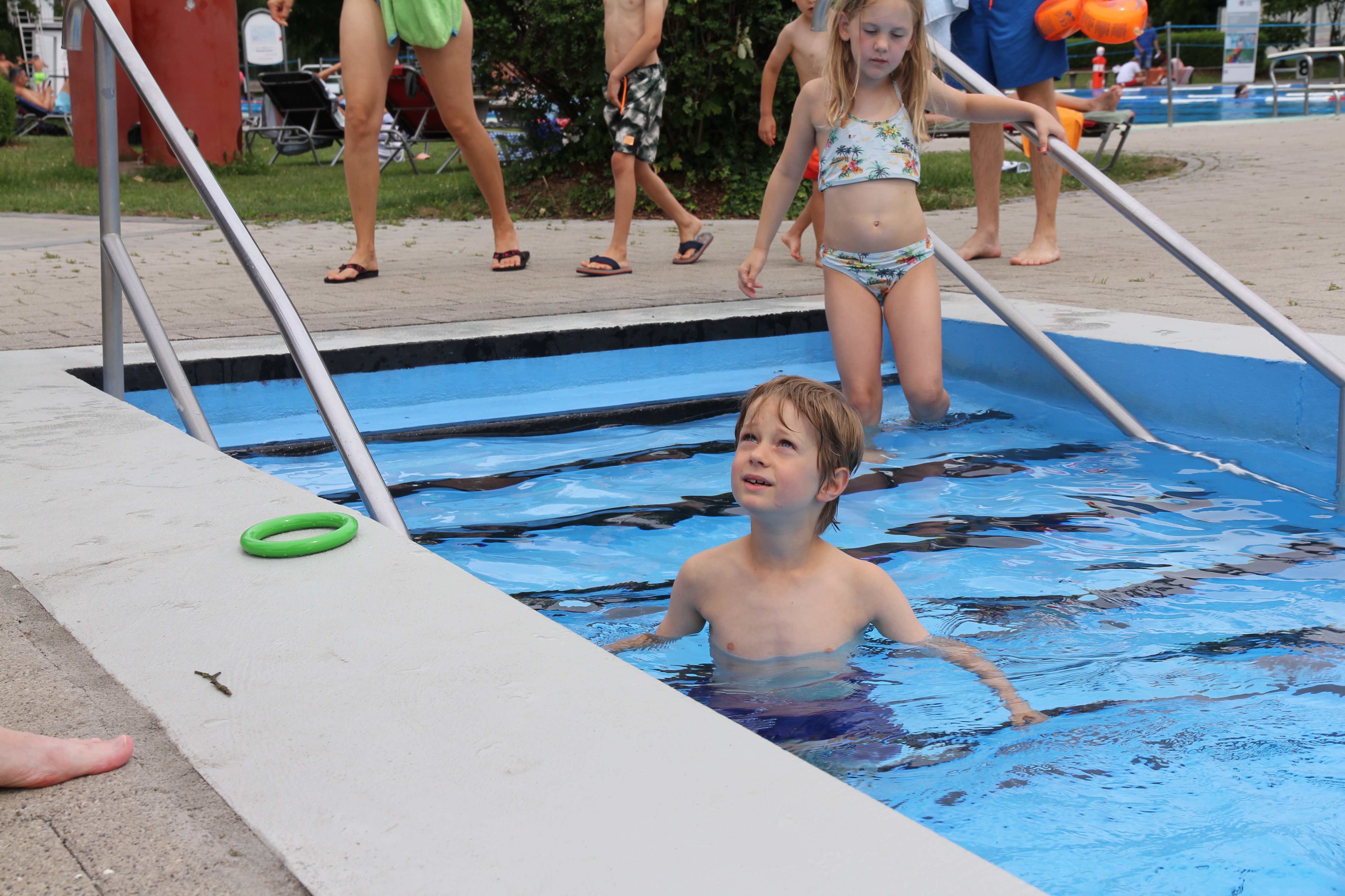 Junge steht im Pool und hört der Wasserwacht zu