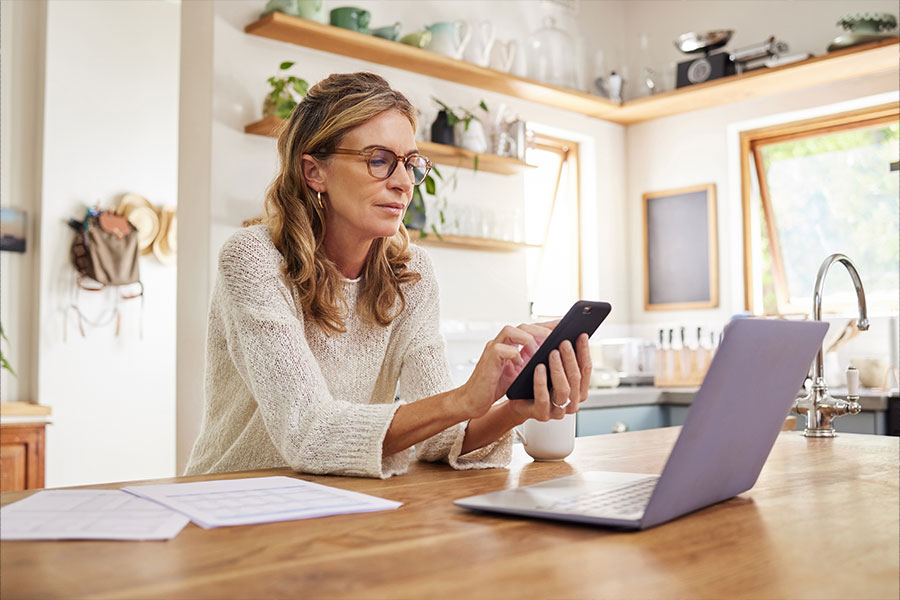 Frau mit Smartphone und Laptop am Schreibtisch