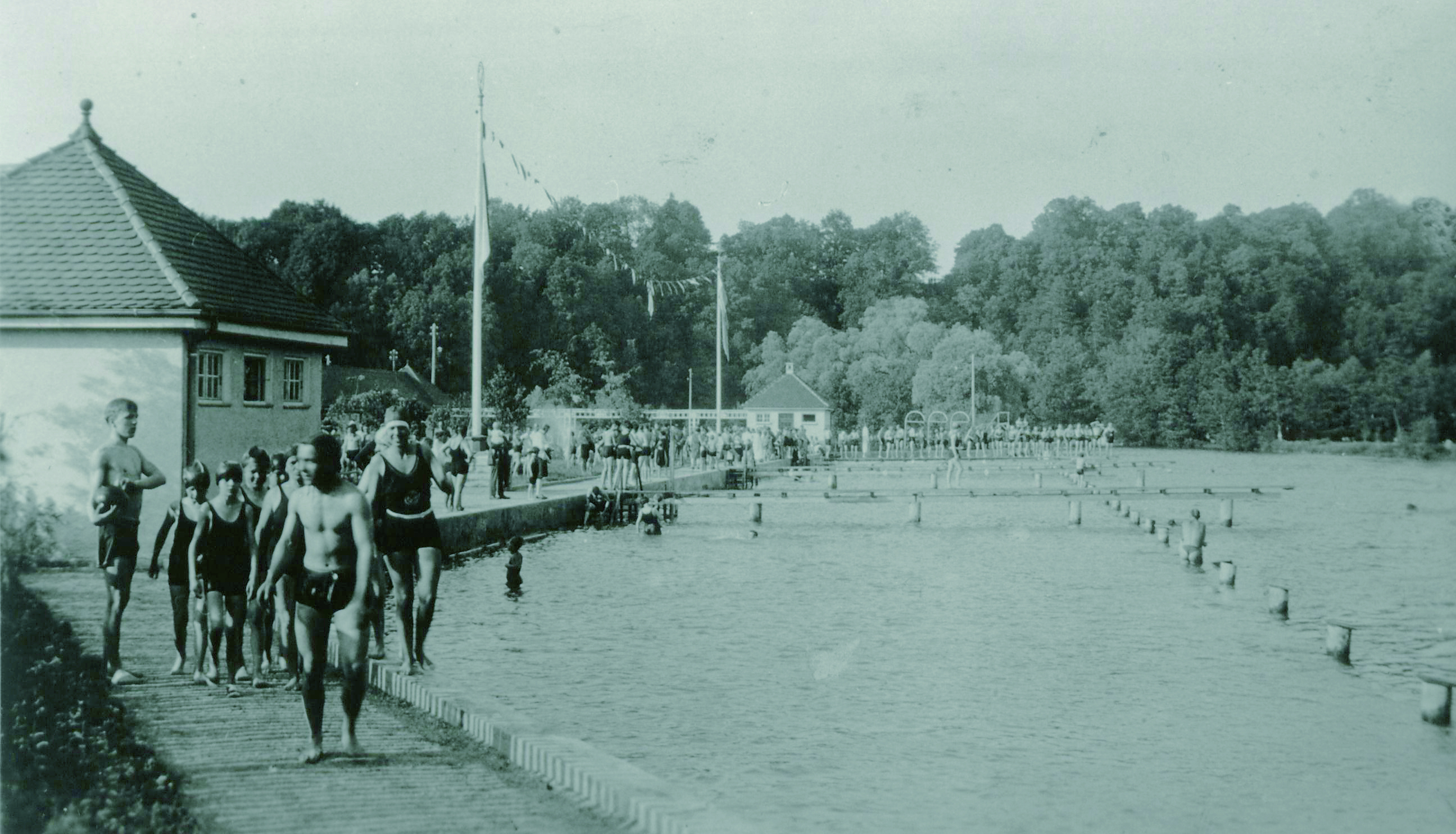 Schwimmbecken und Gebäude des Dachauer Freibads aus den 1930er Jahren, Personen in Badekleidung im Vordergrund